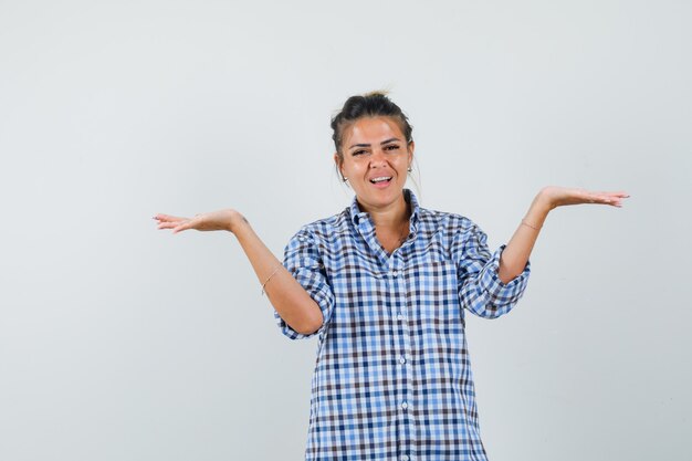 Young woman showing helpless gesture in checkered shirt and looking dissatisfied.