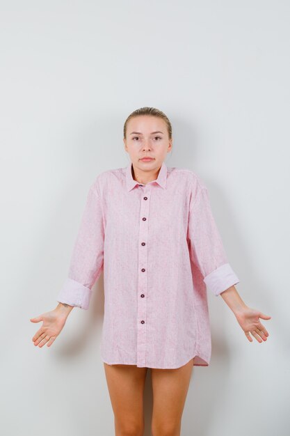 Young woman showing helpless gesture in pink shirt and looking confused