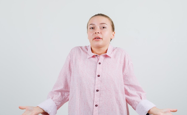 ピンクのシャツで無力なジェスチャーを示す若い女性