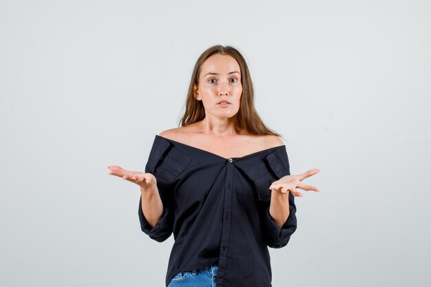 Young woman showing helpless gesture in shirt, shorts and looking confused. front view.