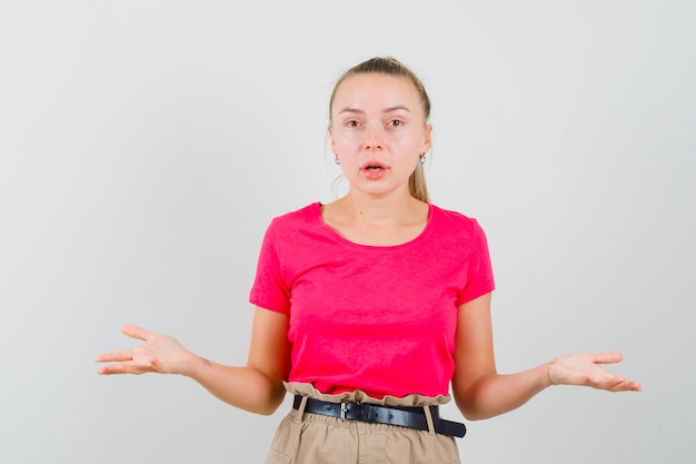 Young woman showing helpless gesture in t-shirt and pants and looking confused
