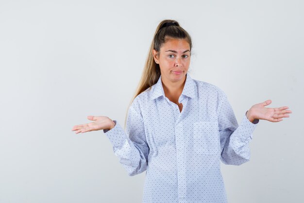 Young woman showing helpless gesture in white shirt and looking puzzled
