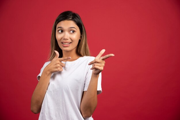 Young woman showing her fingers on red wall.