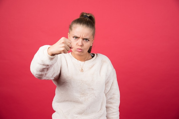 Young woman showing her fist on a red wall