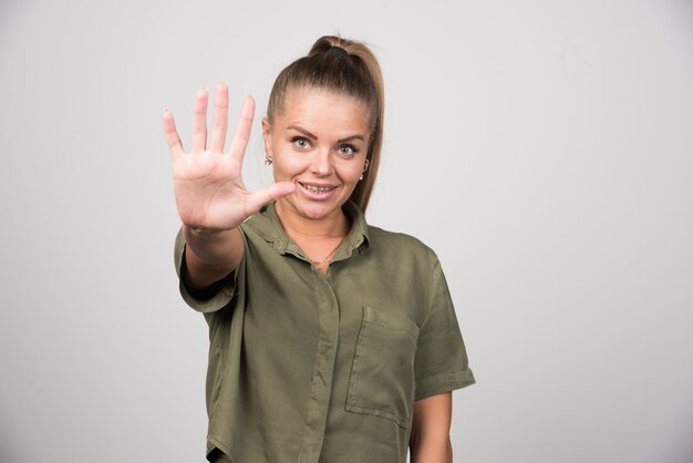 Young woman showing her hand on gray wall.