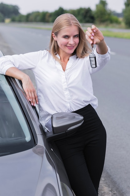 車のミディアムショットのキーを示す若い女性