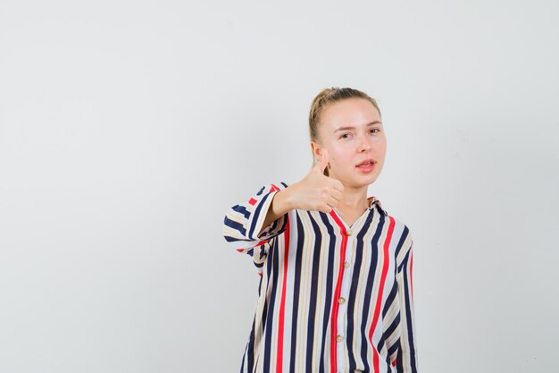 Young woman showing like gesture in striped blouse and looking happy