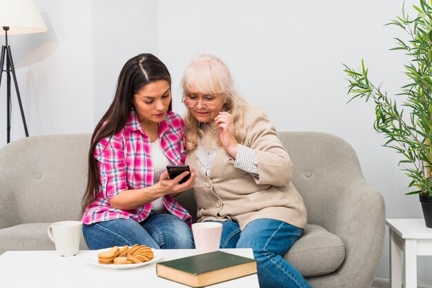 Young woman showing mobile to her mother sitting on sofa