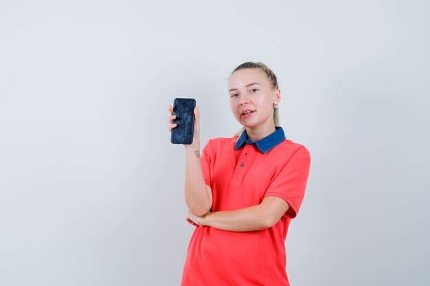 Young woman showing mobile phone in t-shirt and looking pleased