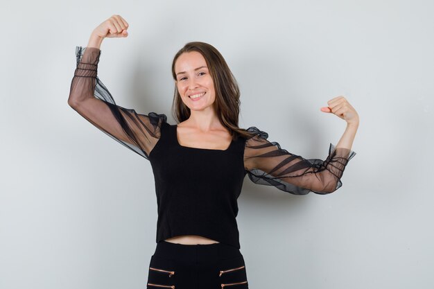 Young woman showing muscles in black blouse and black pants and looking confident. front view.