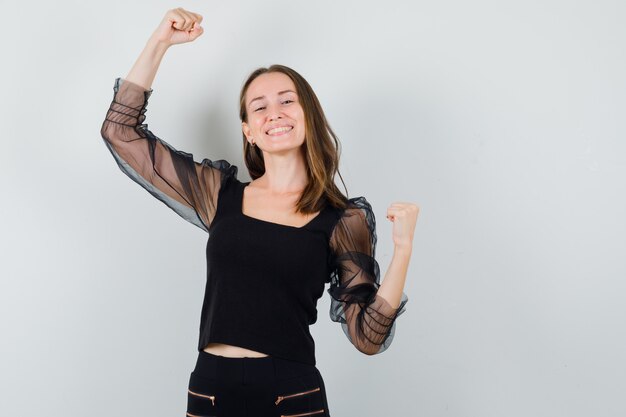 Young woman showing muscles and smiling in black blouse and black pants and looking confident 