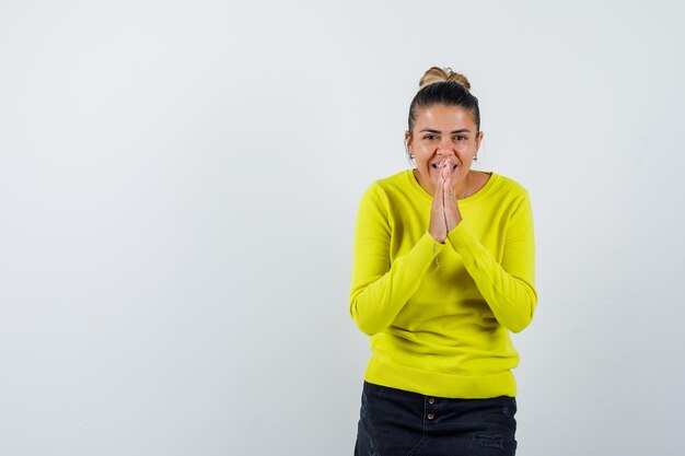 Young woman showing namaste gesture in yellow sweater and black pants and looking happy