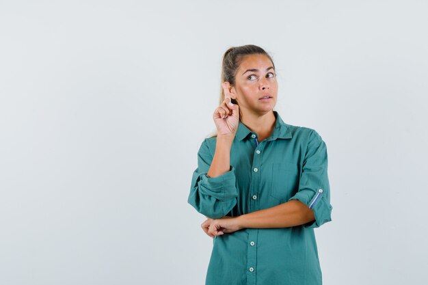 Free photo young woman showing new idea gesture in blue shirt and looking pensive