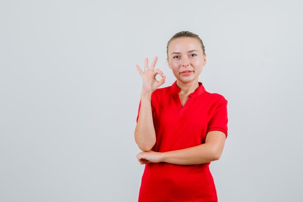 Young woman showing ok gesture in red t-shirt and looking pleased
