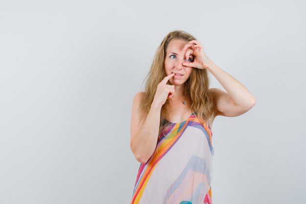 Young woman showing ok sign on eye while looking away in summer dress and looking hopeful 