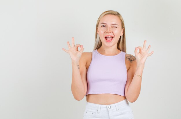 Молодая женщина показывает знак ОК с морганием в синглете