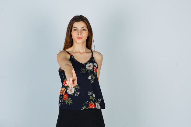 Young woman showing one finger in floral top and looking serious