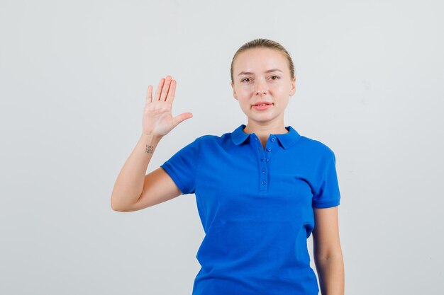 青いTシャツで手のひらを示し、自信を持って見える若い女性