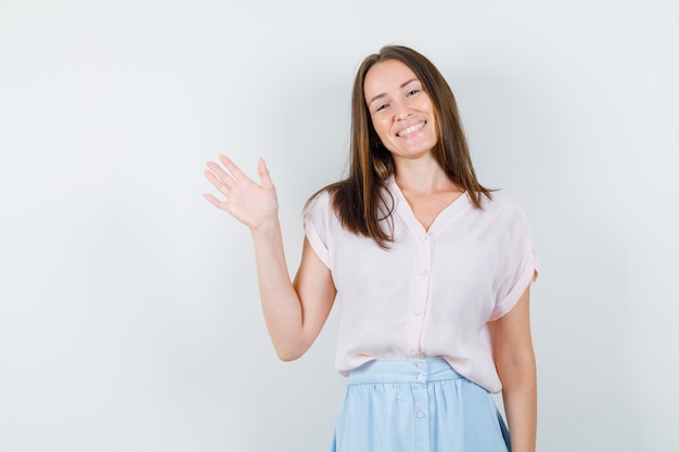 Free photo young woman showing palm in t-shirt, skirt and looking glad. front view.