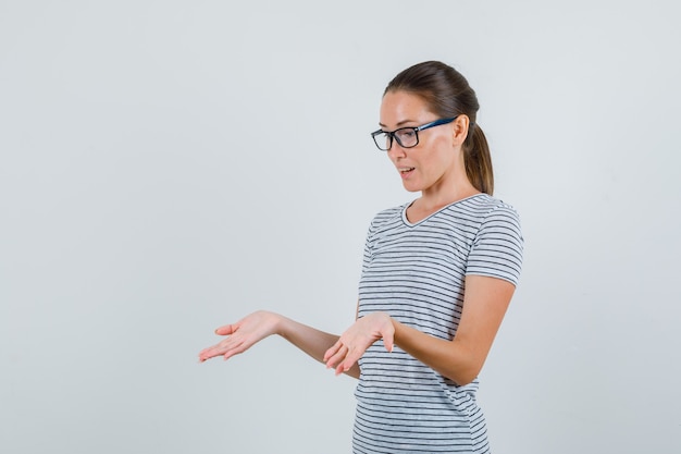 縞模様のTシャツ、メガネで手のひらを見せて、驚いて見える若い女性。正面図。