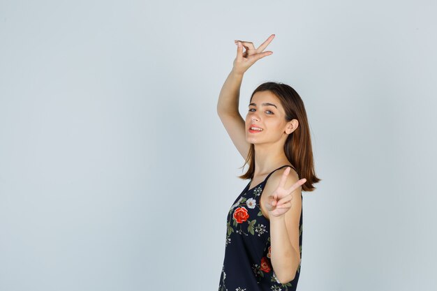 Young woman showing peace gesture in blouse and looking happy .