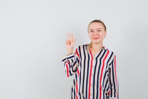 Молодая женщина демонстрирует жест мира в полосатой блузке и выглядит оптимистично
