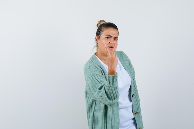 Free photo young woman showing peace sign in white shirt and mint green cardigan and looking serious