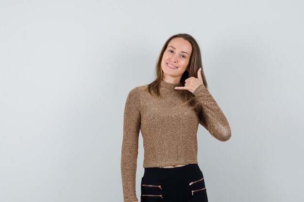 Молодая женщина показывает жест телефона в позолоченном золотом свитере и черных брюках и выглядит счастливой