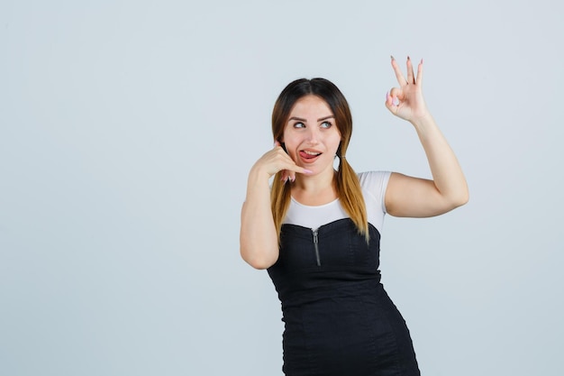 Молодая женщина показывает жест телефона и знак ОК, высунув язык