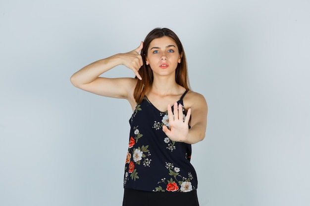 Free photo young woman showing phone gesture and stop sign in blouse and looking serious. front view.