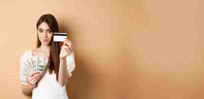 Free photo young woman showing plastic credit card prefer contactless payment instead of dollar bills standing