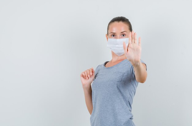 Young woman showing refusal gesture in t-shirt, mask and looking serious , front view.