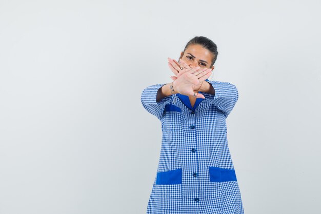 Young woman showing restriction sign in blue gingham pajama shirt and looking serious. front view.