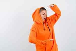 Foto gratuita giovane donna che mostra le squame in felpa con cappuccio arancione e sembra concentrata