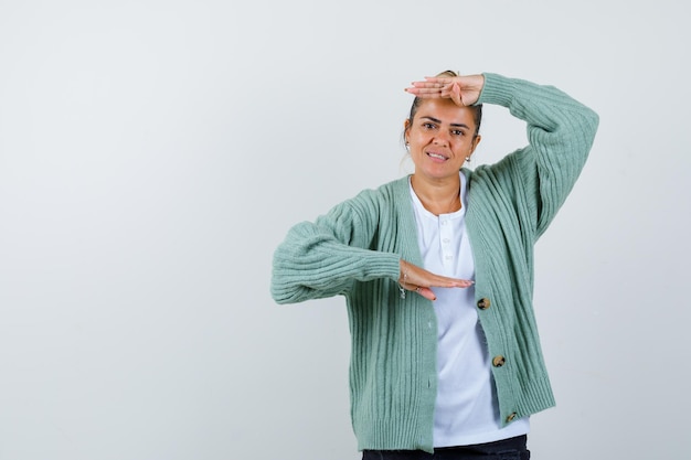 Giovane donna che mostra le squame in maglietta bianca e cardigan verde menta e sembra felice