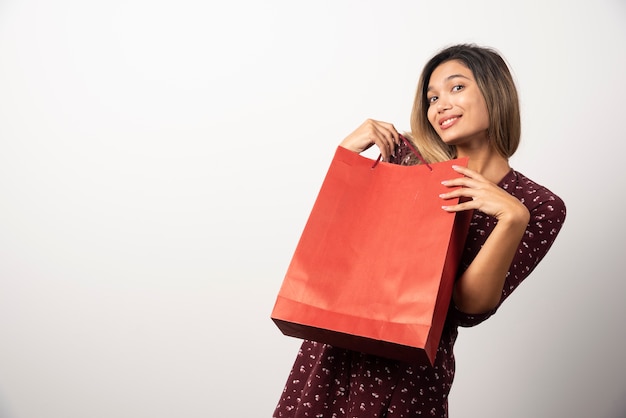 흰 벽에 쇼핑백을 보여주는 젊은 여자.
