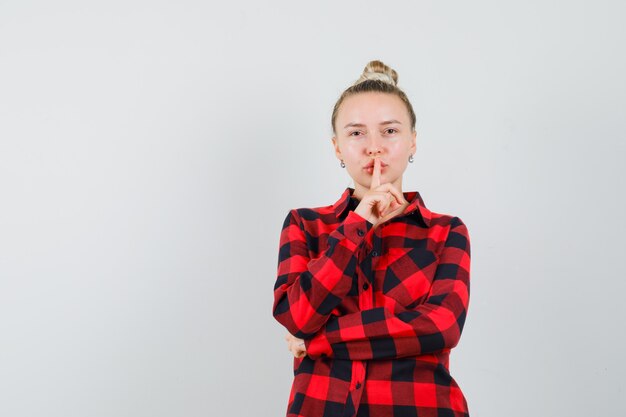 Young woman showing silence gesture in checked shirt and looking careful