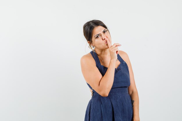 Young woman showing silence gesture in dress and looking careful