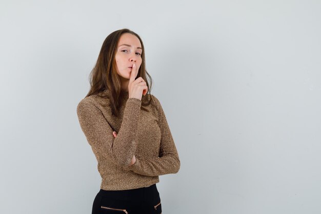 Young woman showing silence gesture in golden blouse and looking calm