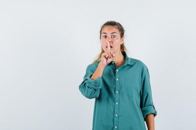 Young woman showing silence gesture in green blouse and looking serious