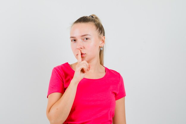 Young woman showing silence gesture in pink t-shirt and looking careful