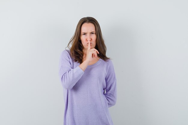 Young woman showing silent gesture in lilac blouse and looking focused. front view.