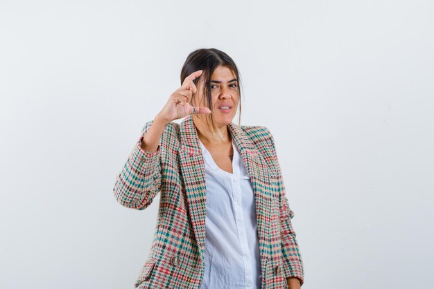 Young woman showing something small hand gesture on white background