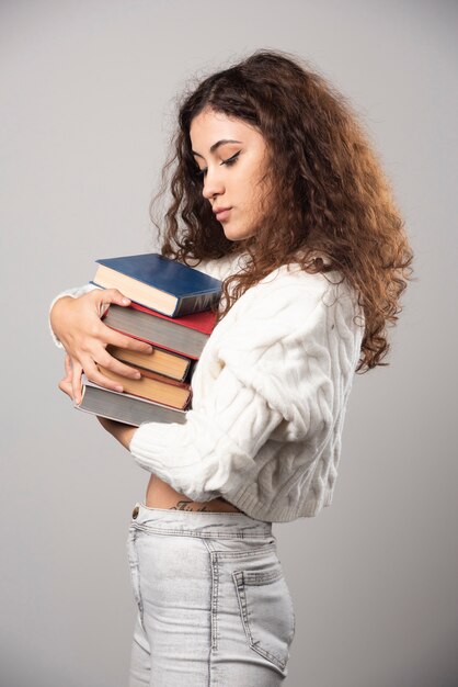 Young woman showing at a stack of books on a gray wall. High quality photo