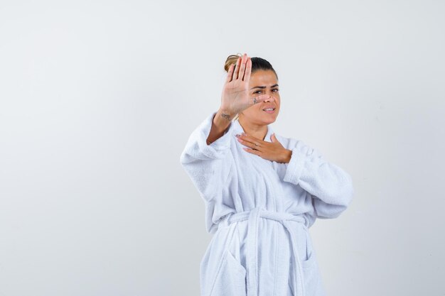 Young woman showing stop gesture in bathrobe and looking confident