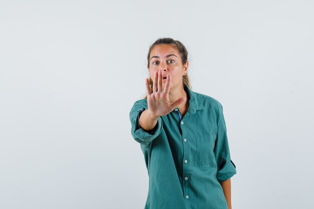Young woman showing stop gesture in blue shirt and looking troubled