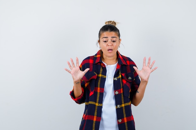 Young woman showing stop gesture in checkered shirt and looking upset , front view.