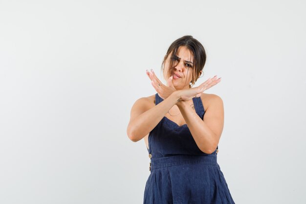 Young woman showing stop gesture in dress and looking annoyed