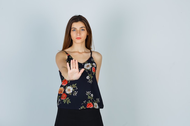 Молодая женщина показывает жест стоп в цветочном топе и выглядит уверенно