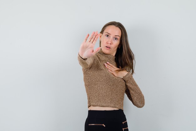 Young woman showing stop gesture in golden blouse and looking serious